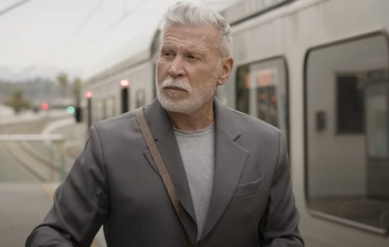 Nick Wooster in a gray suit waits at a light rail station