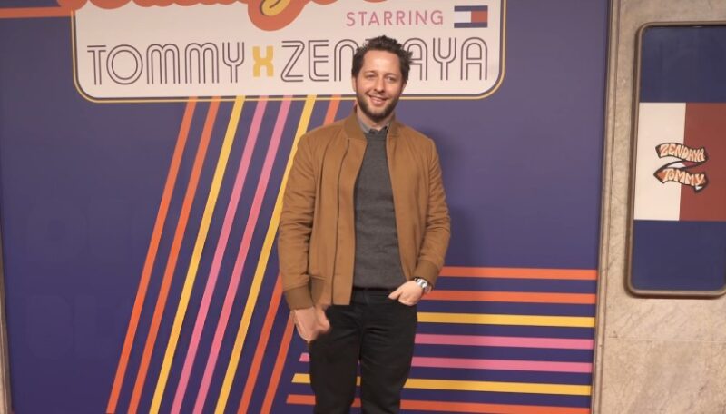 Derek Blasberg in a tan jacket, posing for a Tommy x Zendaya event