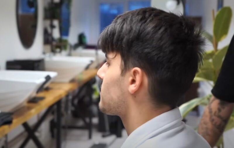 A stylish haircut in progress, the soft cascade of dark hair framing a young man's face
