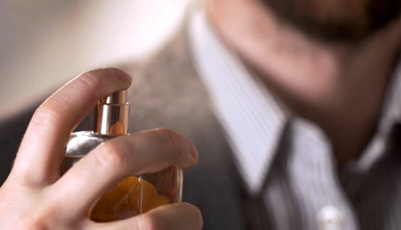 A man carefully applies cologne to his neck
