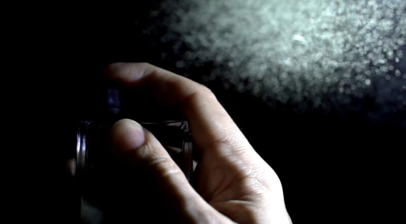 A hand holds a perfume bottle, releasing a fine mist into the air