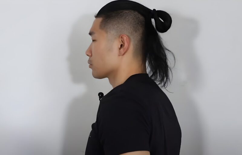 A man with a sleek, high-and-tight haircut and a long, tied ponytail