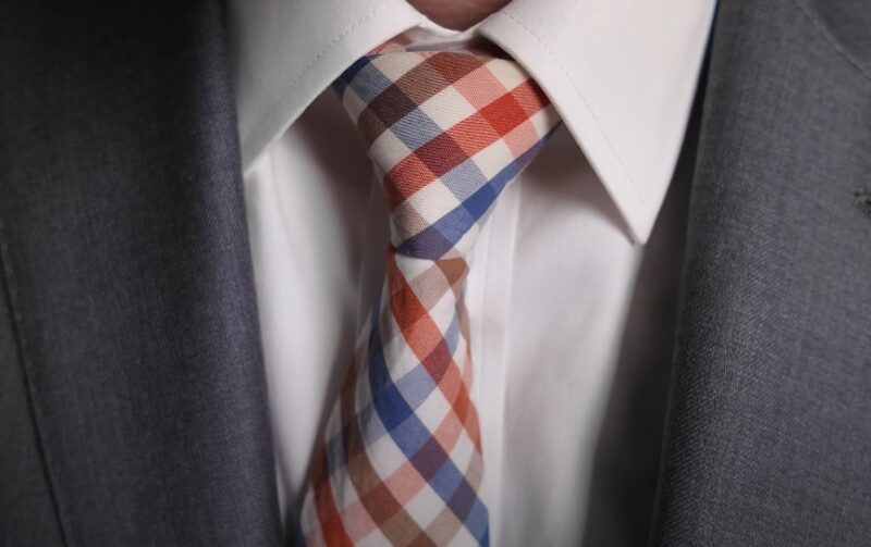 A meticulously knotted tie, a vibrant plaid of orange