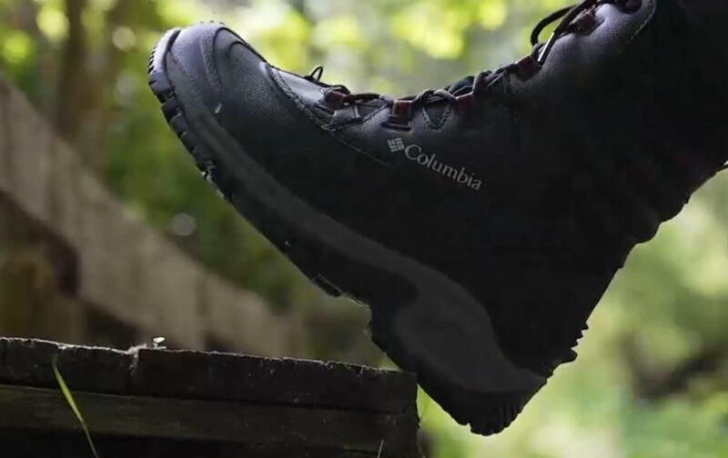 A person in black hiking boots sits on a wooden bench in an outdoor setting