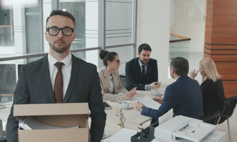 A man in a suit holds a box while standing in front of a group of people
